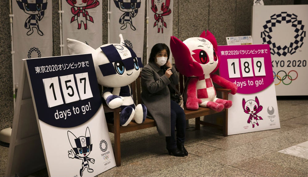 Mujer con tapabocas junto a las mascotas de Tokio 2020