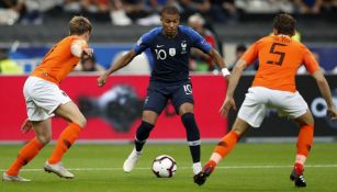Kylian Mbappé intenta pasar entre dos defensores de Holanda
