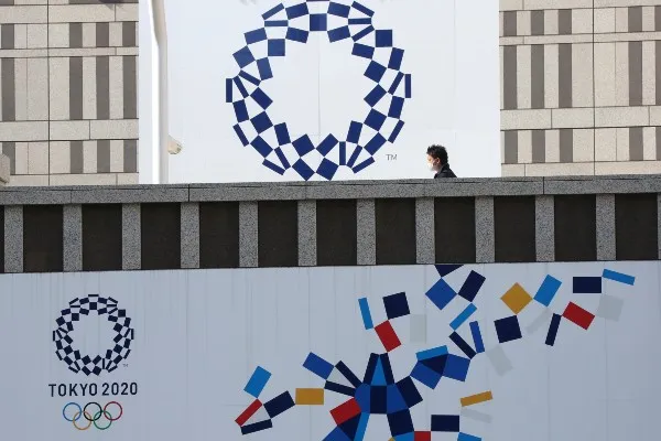 Un hombre con mascarilla camina frente al logotipo de los Juegos Olímpicos de Tokio