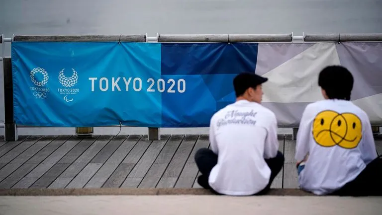 Personas enfrente de un cartel de Tokio 2020