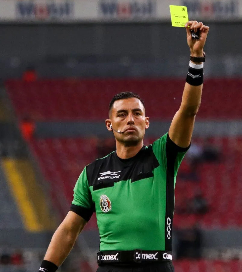 El árbitro Brian Omar González muestra la tarjeta amarilla