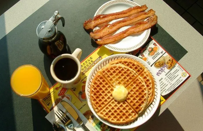Waffle acompañado de miel y a un costado un plato con tocino