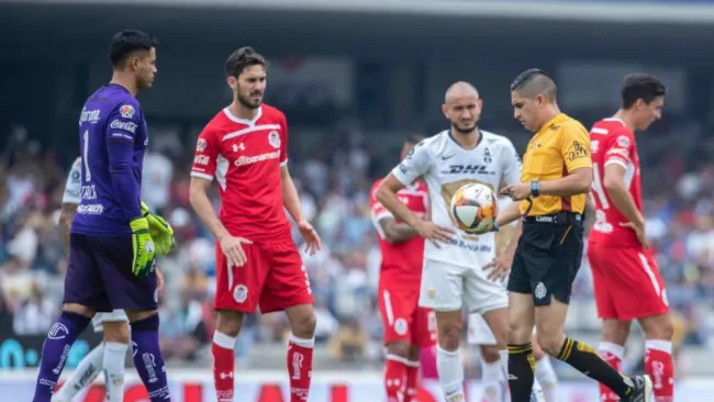 Árbitro toma el balón durante el partido