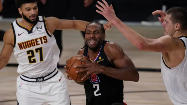Kawhi Leonard, de los Clippers de Los Ángeles, avanza entre Jamal Murray