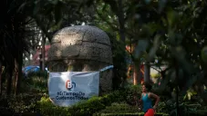 Persona corre frente a cabeza Olmeca con cubrebocas