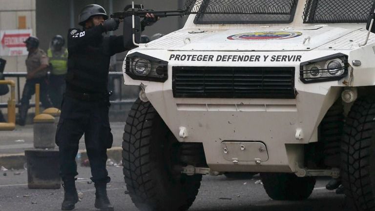 Un policía venezolano se refugia tras un camión, mientras dispara