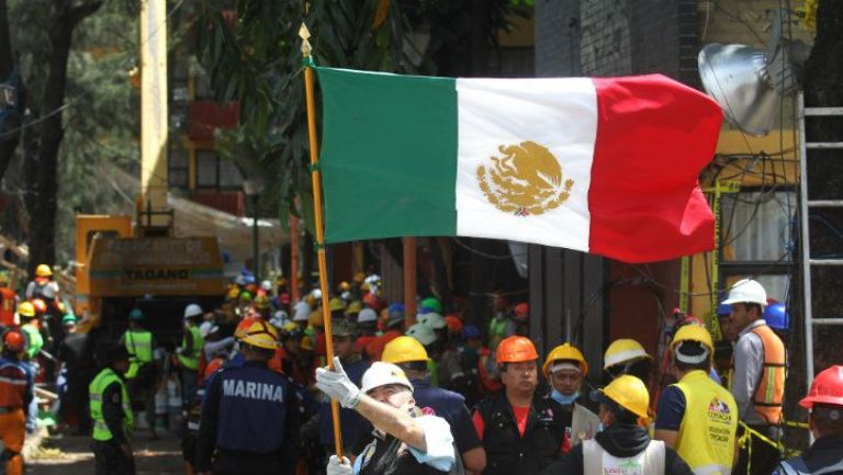 Voluntario ondea la bandera de México durante la remoción de escombros